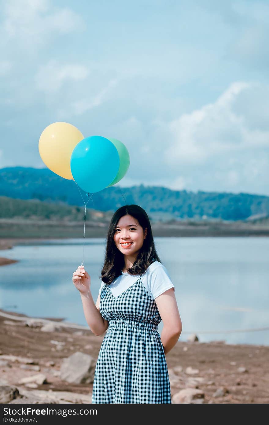 Shallow Focus Photography of Woman in White and Black Short-sleeved Dress Holding Balloons