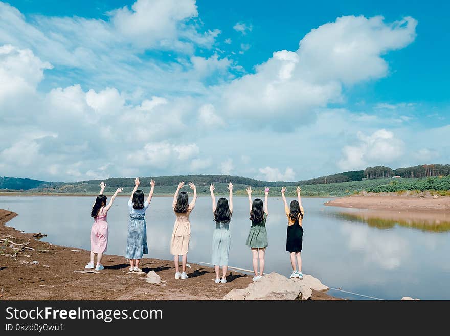 Six Girls Raise Their Hands in Front of Body of Water