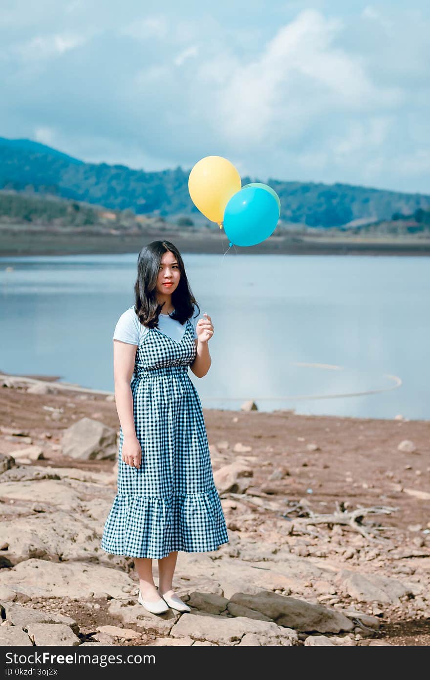 Woman in White and Black Dress Stands While Holding Party Balloons