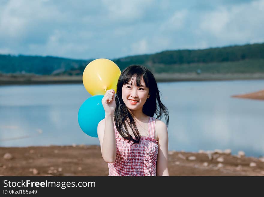 Woman in Pink Thick Strap Top Holding a Yellow and Blue Balloons