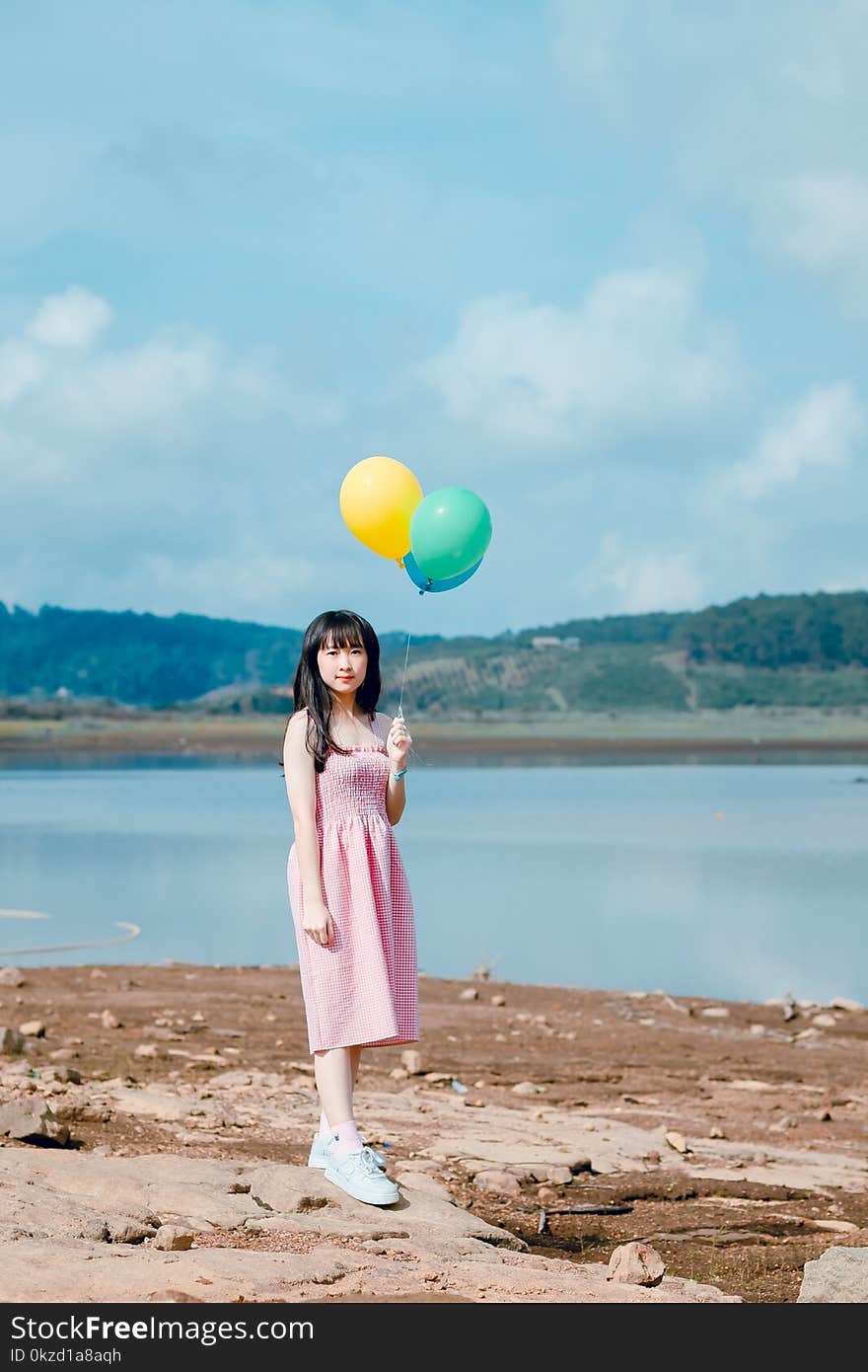 Woman Holding Balloons Standing on Beige Sand