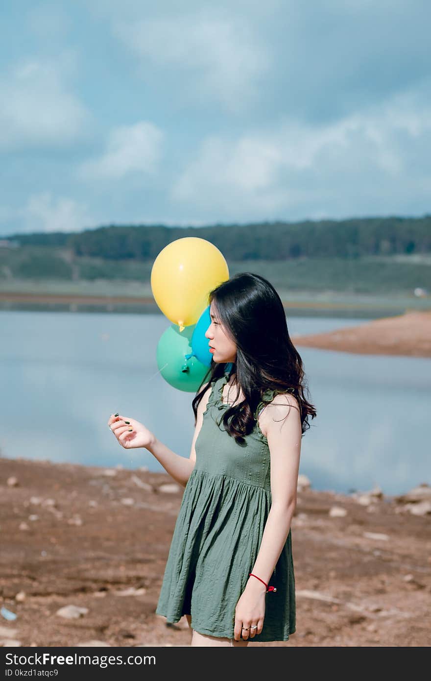 Woman in Green Crew-neck Sleeveless Mini Dress Holding Balloons Near Body of Water