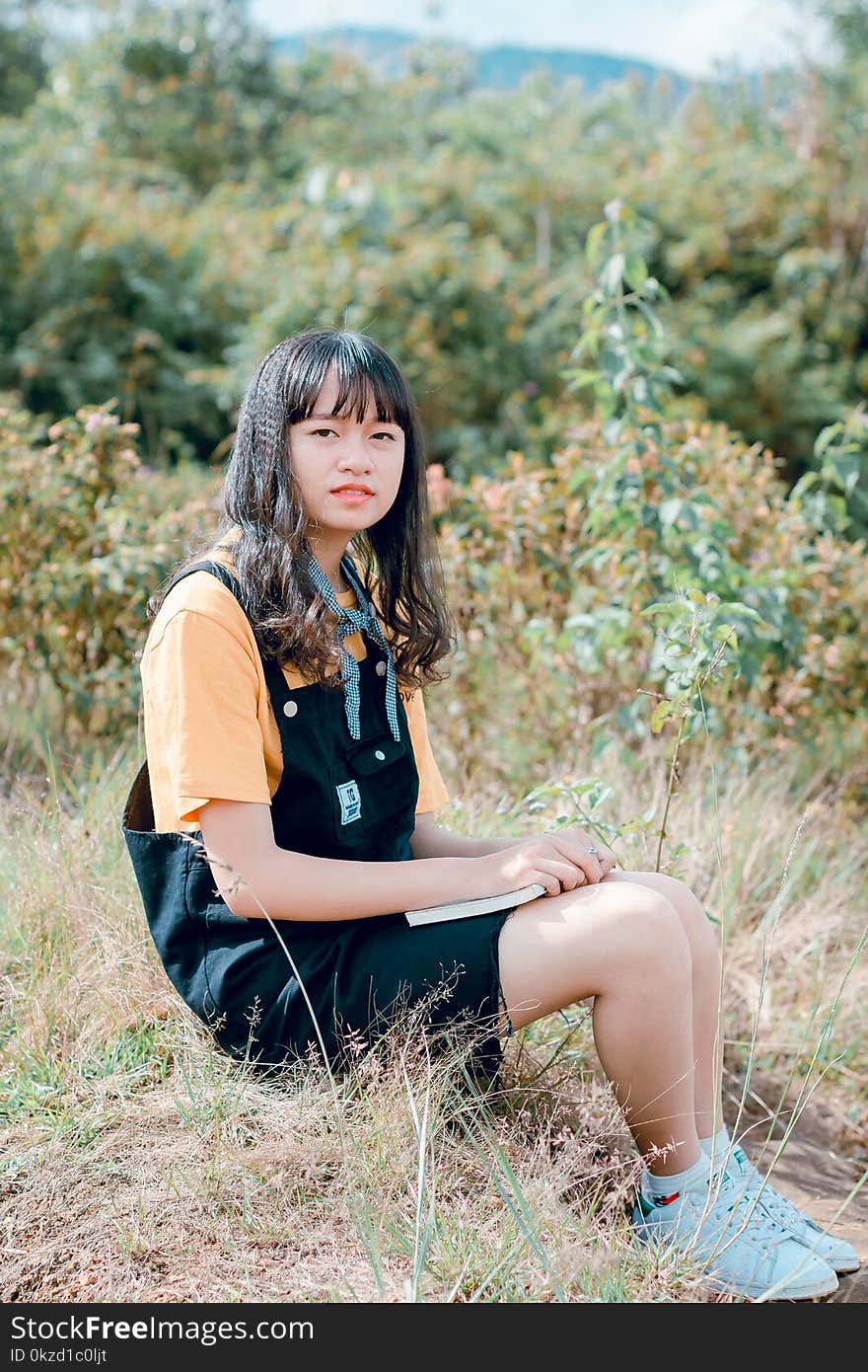 Girl in Black Dungaree and Orange Shirt Sitting of Grass Field