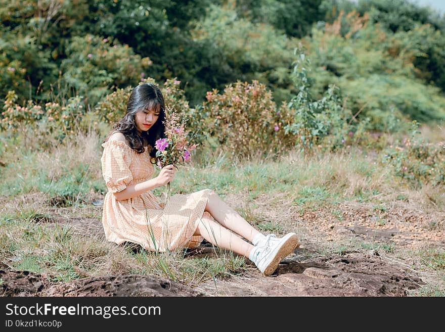 Woman Sitting on Ground and Holding Flower