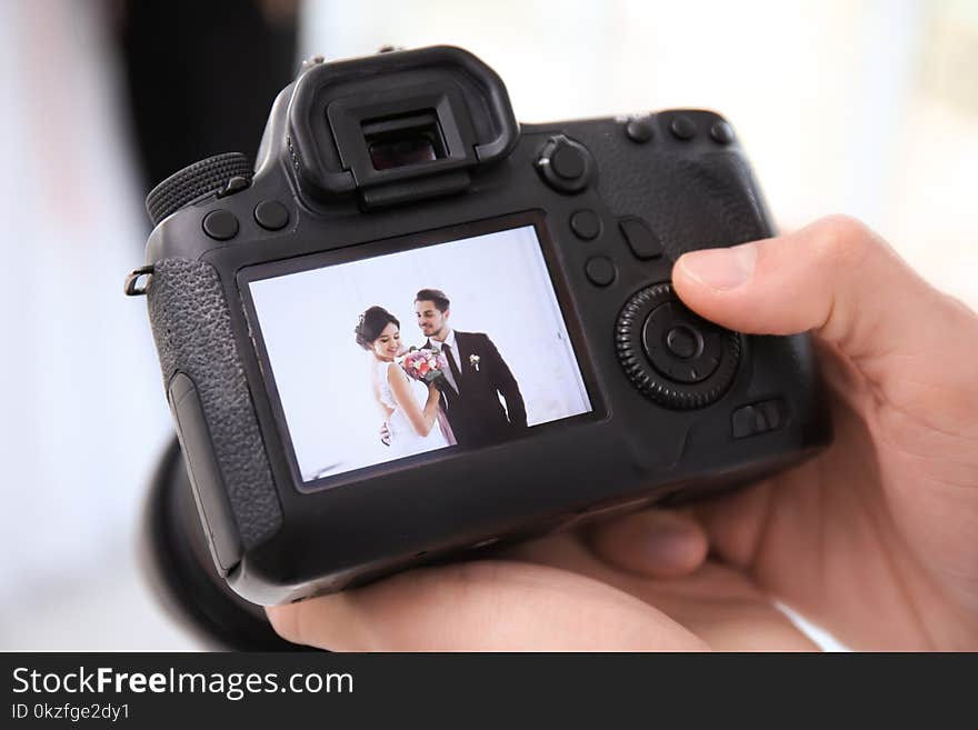 Professional photographer holding camera with lovely wedding couple on display