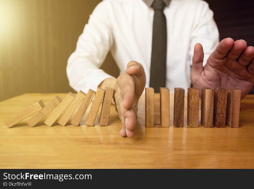 Hand of businessman is stoping falling wooden domino effect from