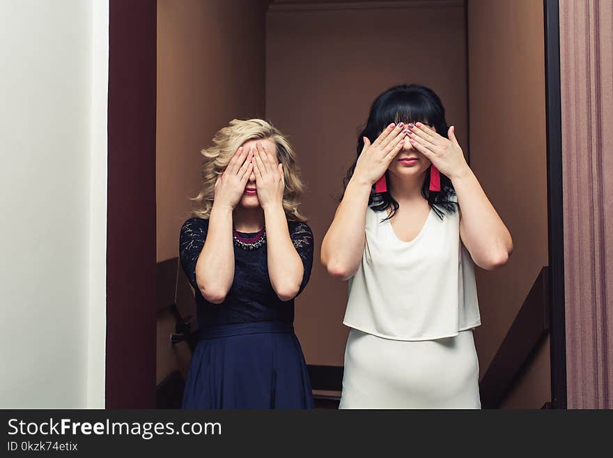 Two Stylish Girls Stand With Eyes Closed With Hands.