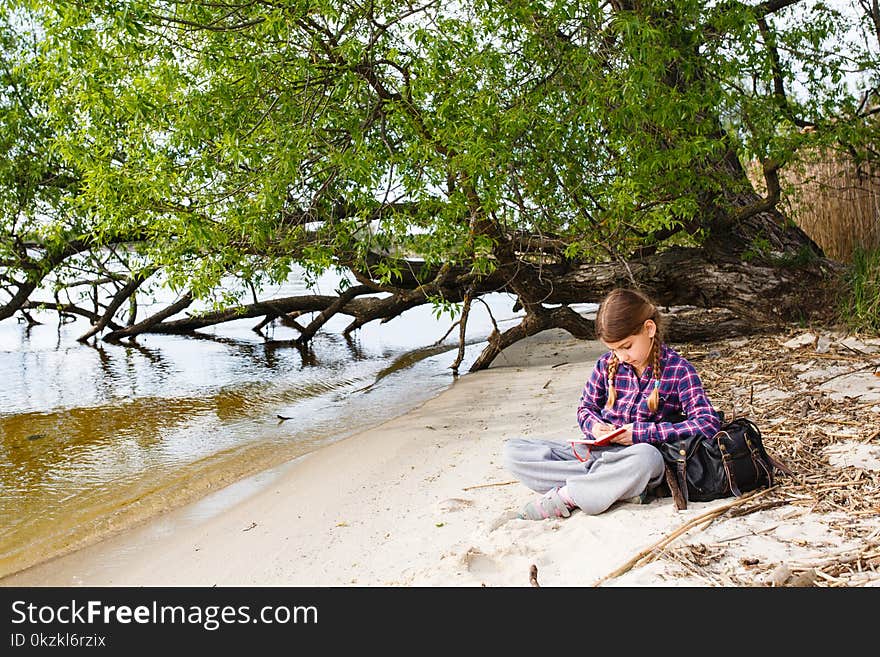 Little girl with backpack relaxing on the beach near by tree at sunny day