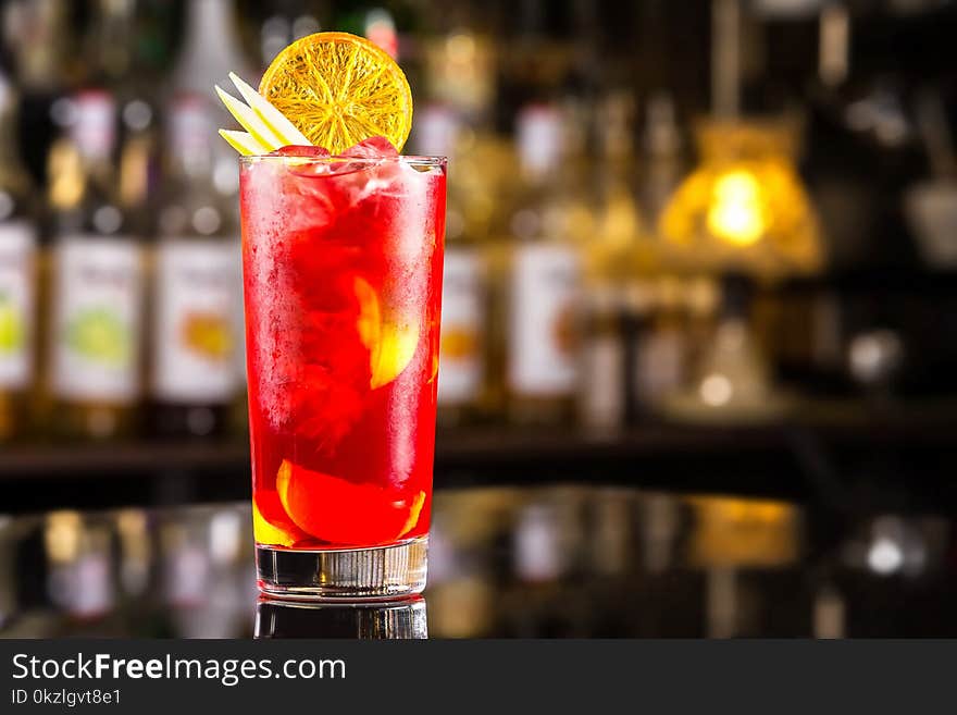 Closeup glass of cocktail with strawberry syrup, rum and lemon decorated with orange slice at bar background.