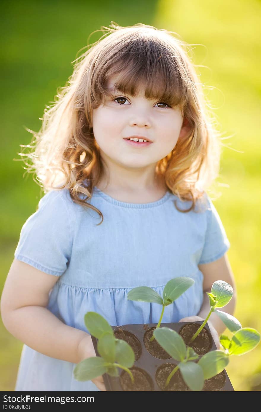 Adorable blond little girl in the greenhouse holding cucumber seedlings in plastic pots, spring garden works. Adorable blond little girl in the greenhouse holding cucumber seedlings in plastic pots, spring garden works.