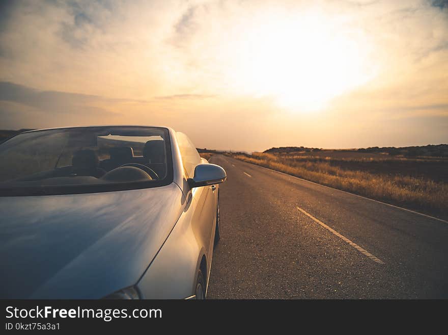 Travelling. Fashionable luxury empty car with open roof is parking on road. Wonderful sunset with sky in background. Copy space in the right e. Travelling. Fashionable luxury empty car with open roof is parking on road. Wonderful sunset with sky in background. Copy space in the right e