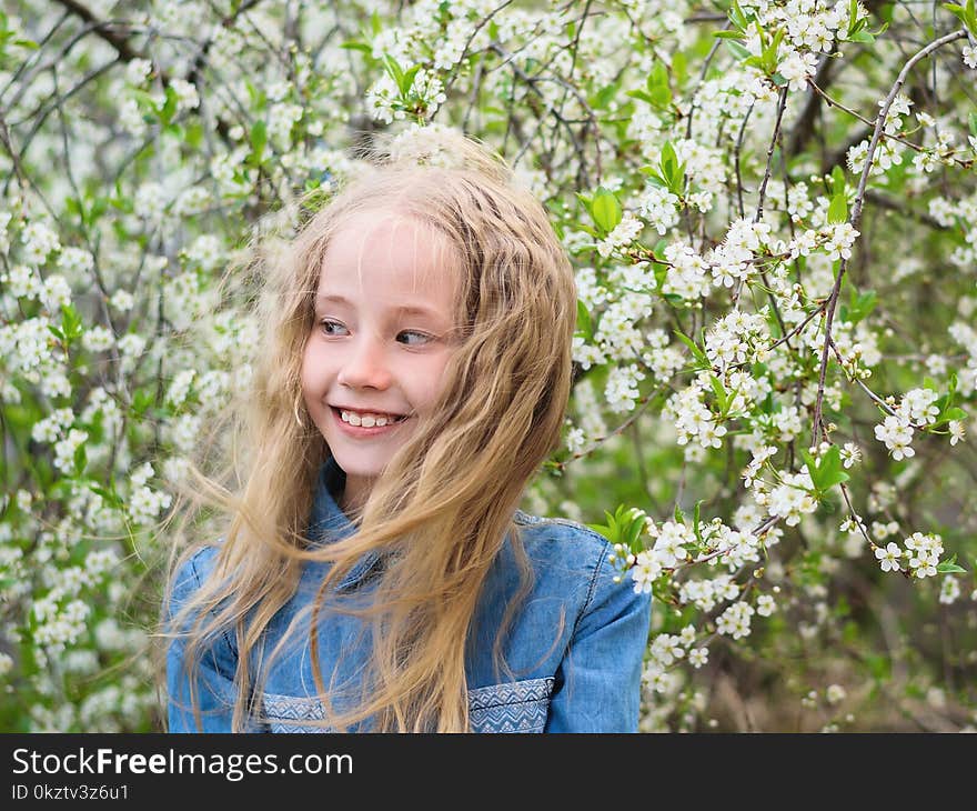 Portrait of a beautiful girl in a denim shirt next to a cherry tree. Portrait of laughing happy girl.