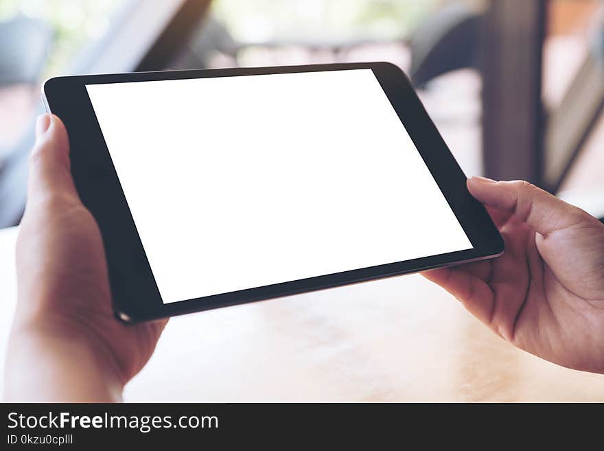 Mockup image of hands holding and using a black tablet pc with blank white desktop screen