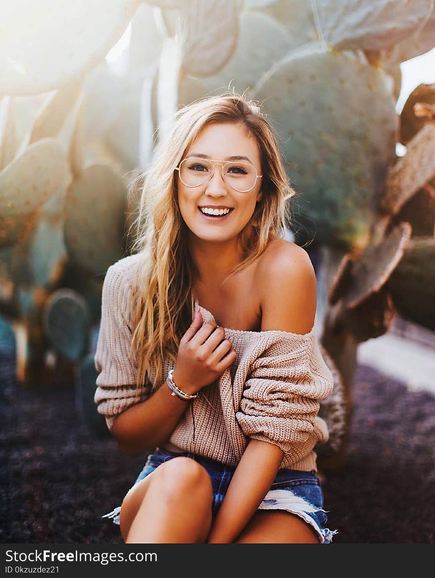 Woman In Brown Sweater And Distressed Blue Denim Shorts Beside Green Cactus