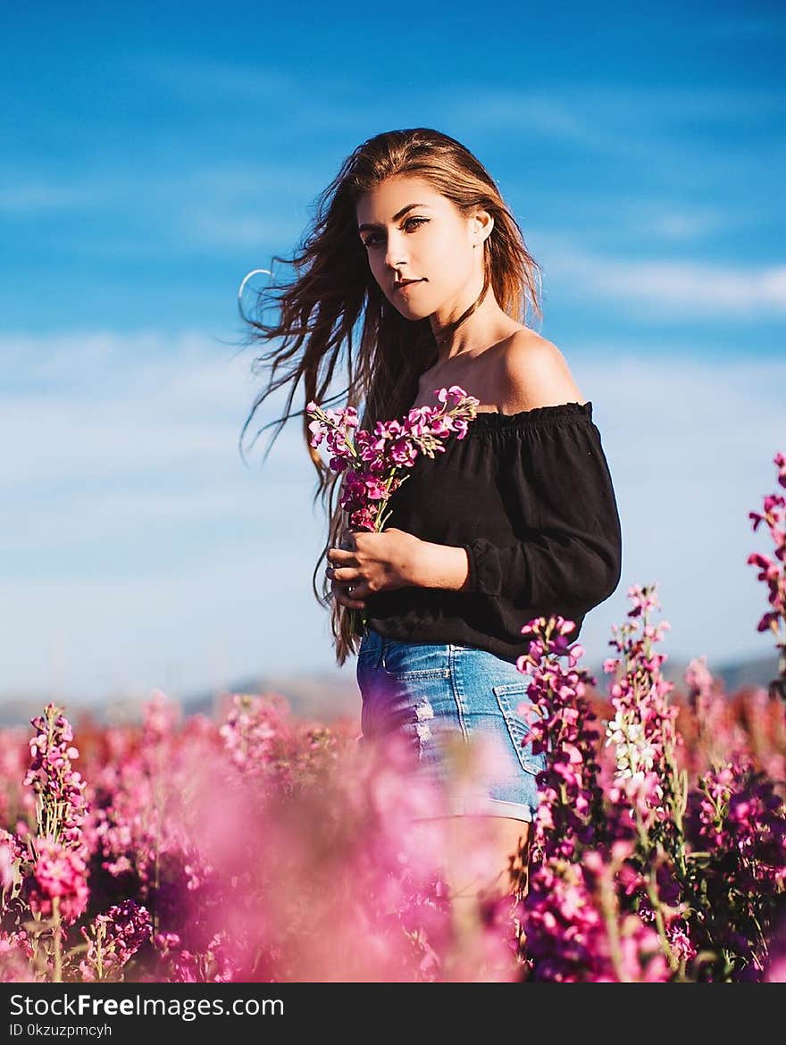 Woman in Black Long-sleeved Off-shoulder Top and Blue Denim Short Shorts Holding Flowers