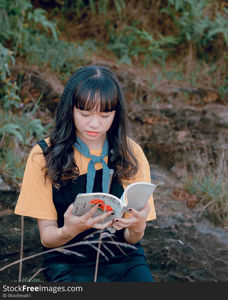 Woman in Orange and Black Top Holding White Book