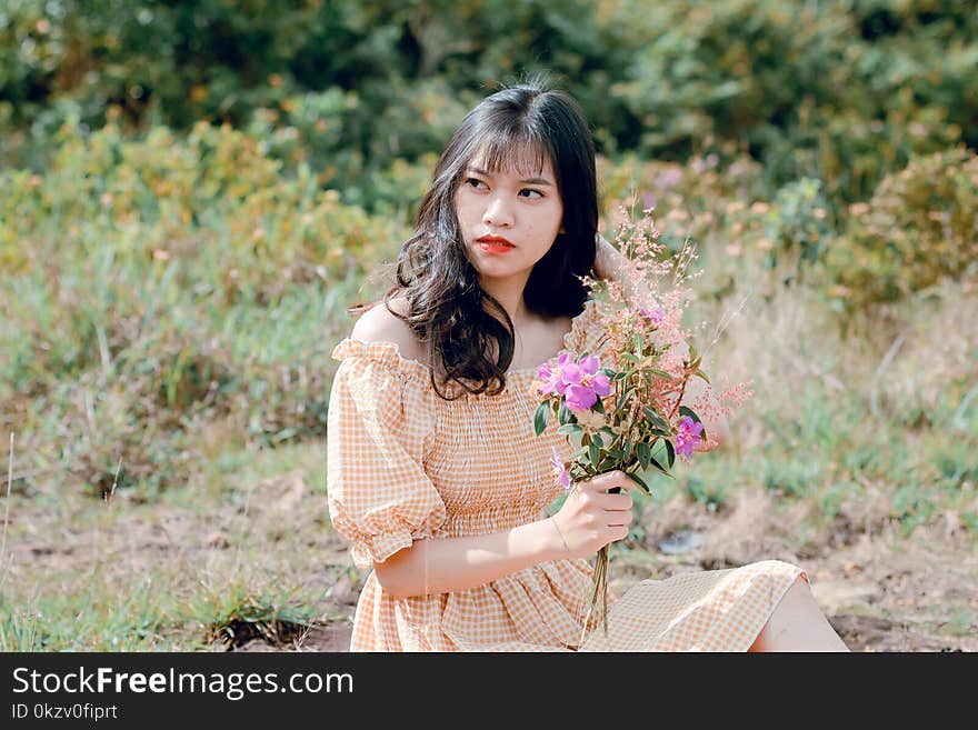 Woman in Orange and White Tattersaal Off-shoulder Dress Holding a Pink Flowers