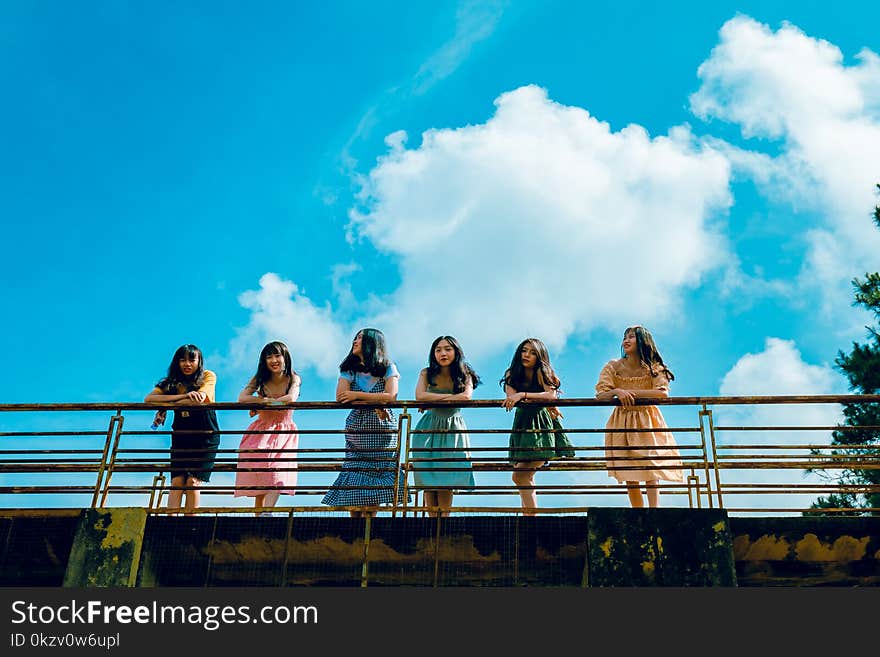 Six Women Wearing Mini Dresses Leaning on Bridge&#x27;s Rail