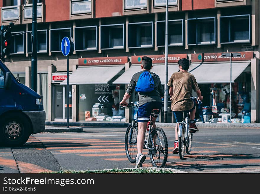 Men Riding Bicycles Traveling on Road Near Red and Gray Building