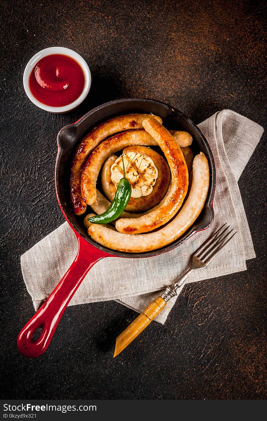 Homemade grilled beef and chicken sausages in red cast iron frying pan, with ketchup, dark background copy space top view. Homemade grilled beef and chicken sausages in red cast iron frying pan, with ketchup, dark background copy space top view