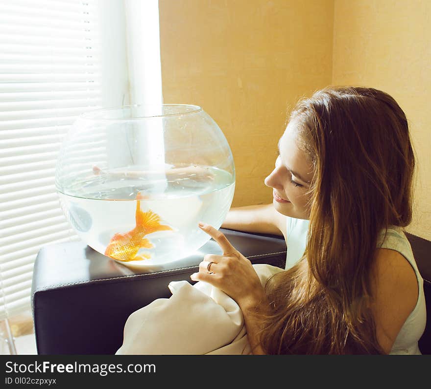 Pretty woman playing with goldfish at home, sunlight morning