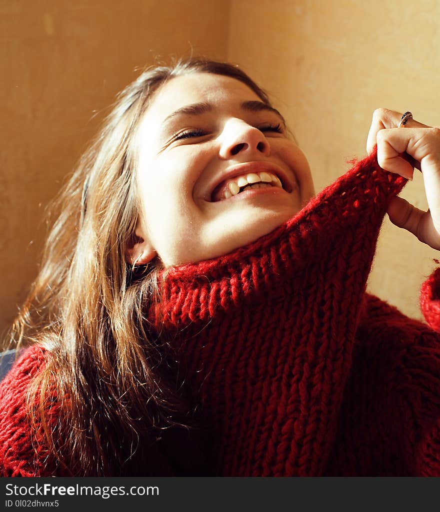 Young pretty real woman in red sweater and scarf all over her face smiling at home, winter positive