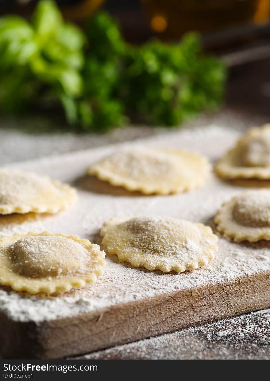 Uncooked tortelli with cheese filling on a wooden board.