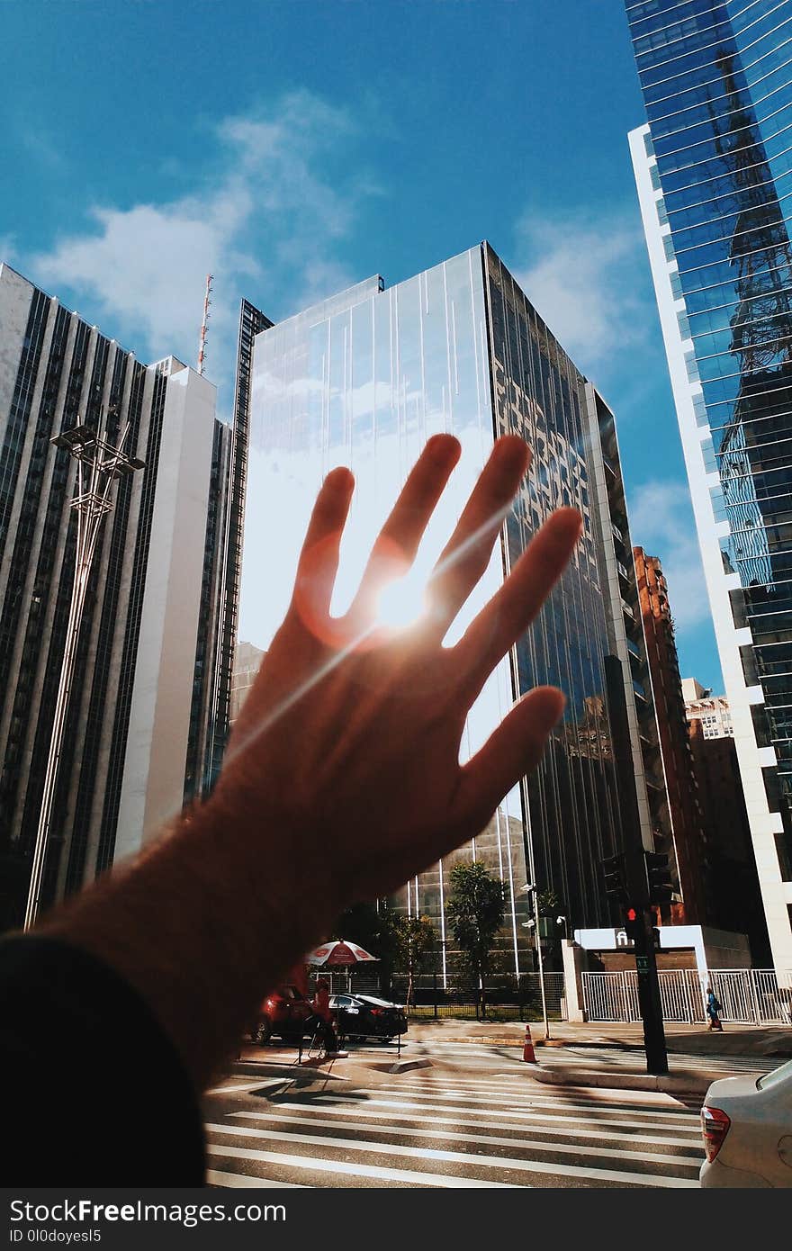 Person Covering the Reflection of Sunlight on Curtain Wall Building at Daytime