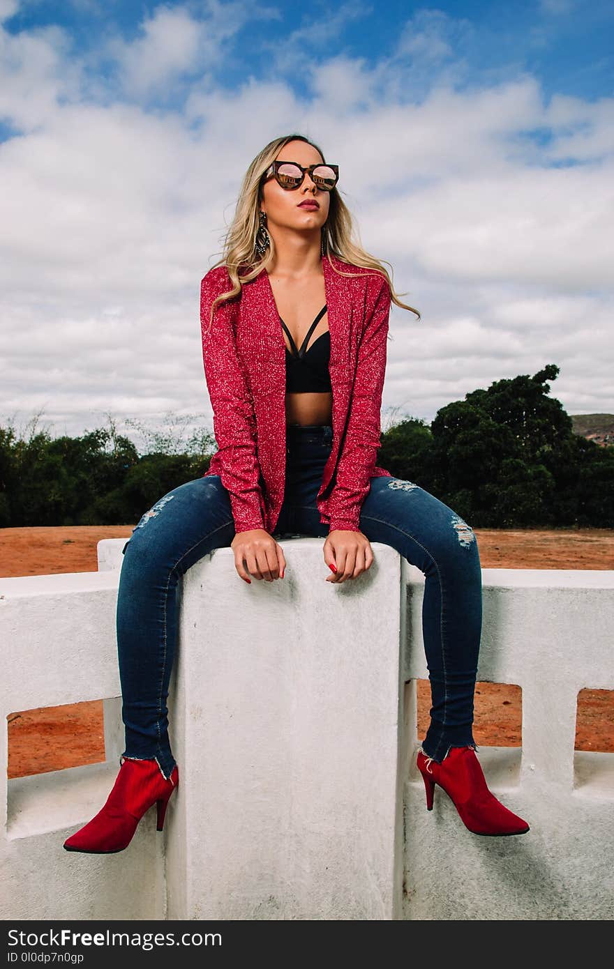 Woman Wearing Red Jacket and Distressed Blue Denim Skinny Jeans Sitting on Bench