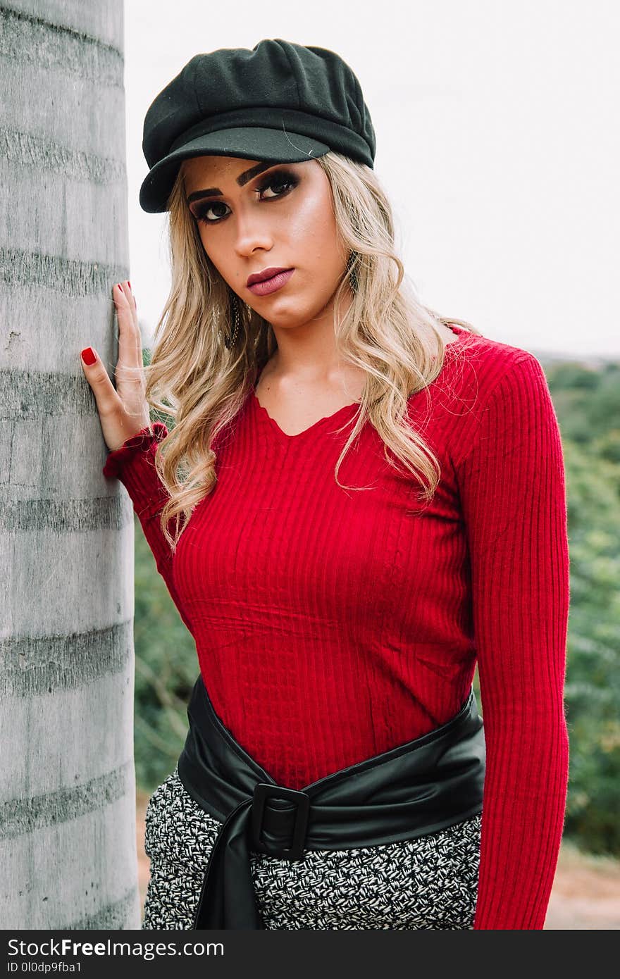 Woman Wearing Black Cap and Red V-neck Sweatshirt Near Concrete Wall