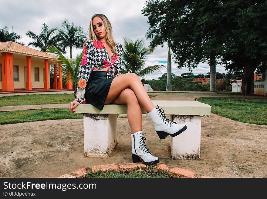 Woman Wearing White and Black Houndstooth Long-sleeved Top and Black Leather Skirt While Sitting on White Concrete Bench