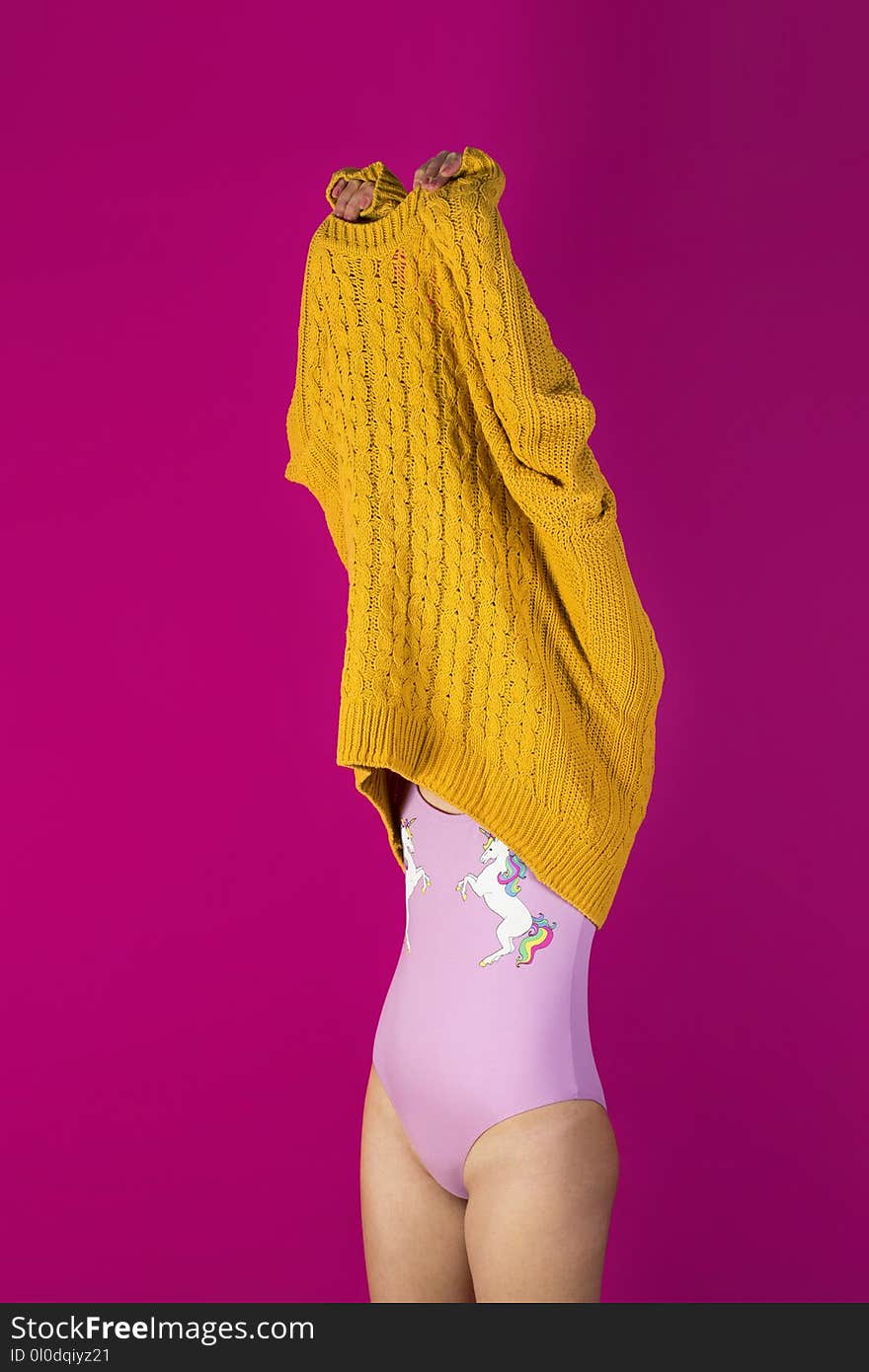 Photo of Woman About to Wear Off Yellow Sweater in Pink Background