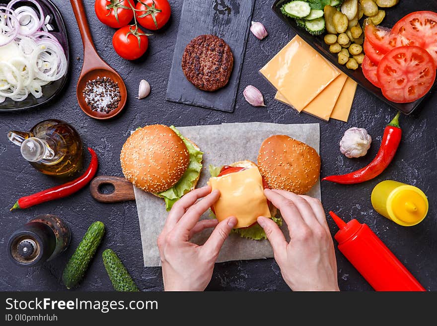Image on top of two hamburgers, human hands and ingredients on black table