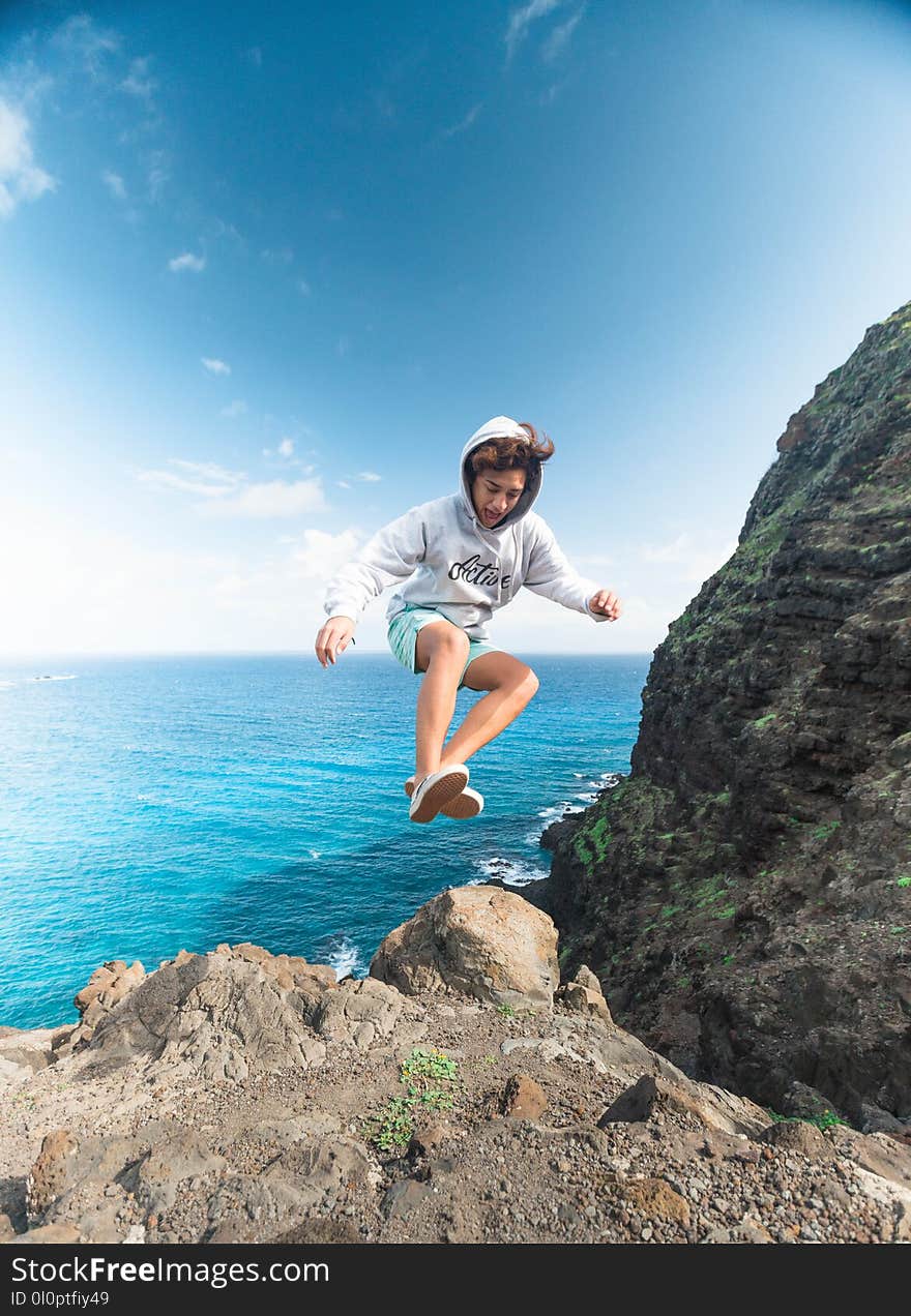 Man Wearing Gray Hoodie Jumping at Rock