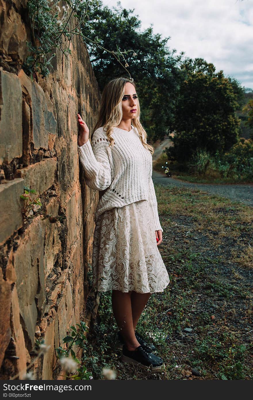 Photo of Woman in White Long-sleeved Shirt Beside Concrete Wall