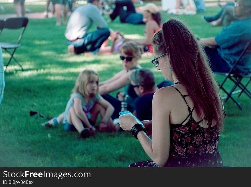 Man Wearing Black and Red Floral Spaghetti-strap Shirt Using Smartphone Sitting on Green Grass at Daytime