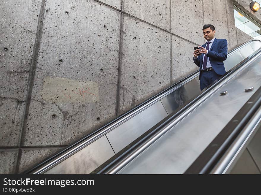 Man Wearing Blue Suit Holding Smartphone on Escalator