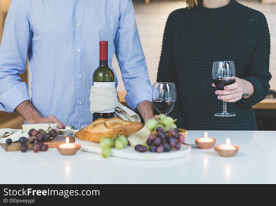 Man Standing Beside Woman Holding Wine Glass in Front of Grapes and Bread on Table