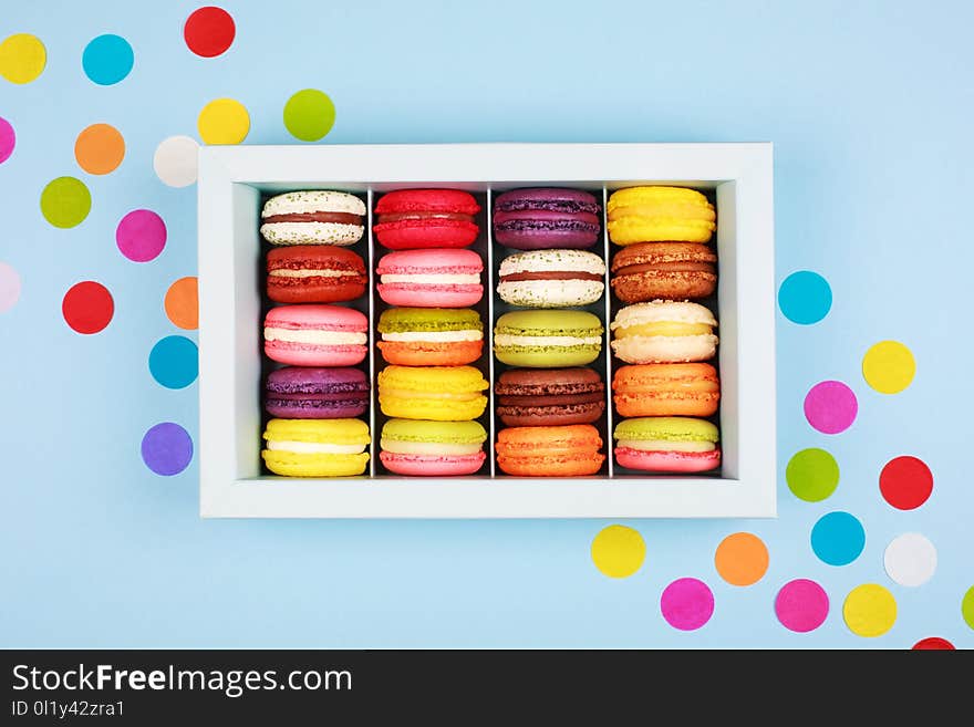 Box of colorful macarons on blue background with confetti. Flat lay style. Box of colorful macarons on blue background with confetti. Flat lay style.