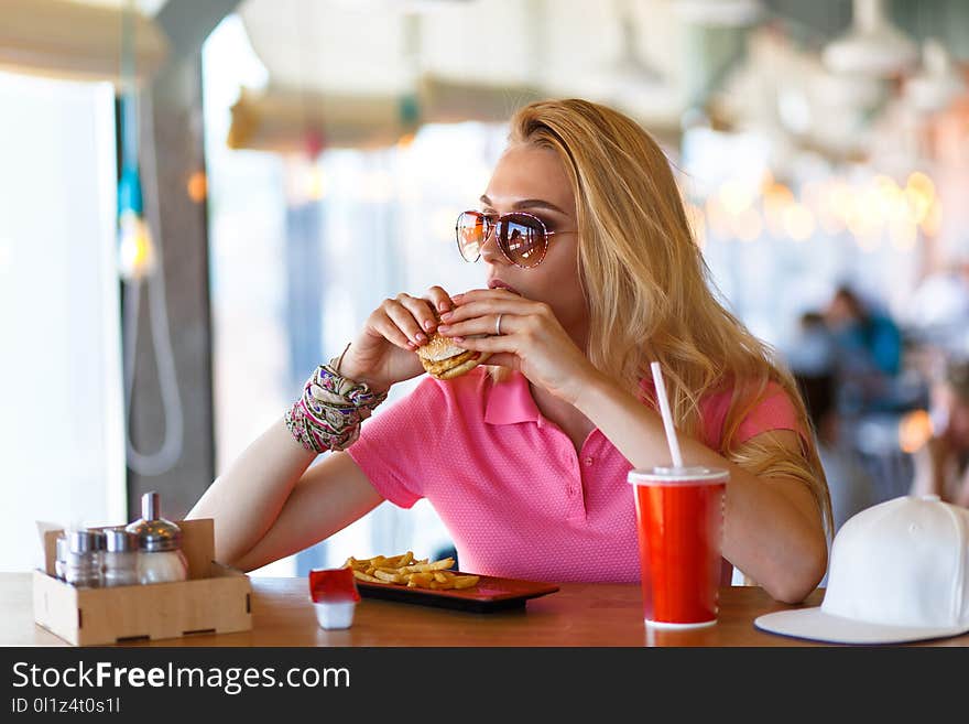 Young pretty woman resting in cafe and eating burger