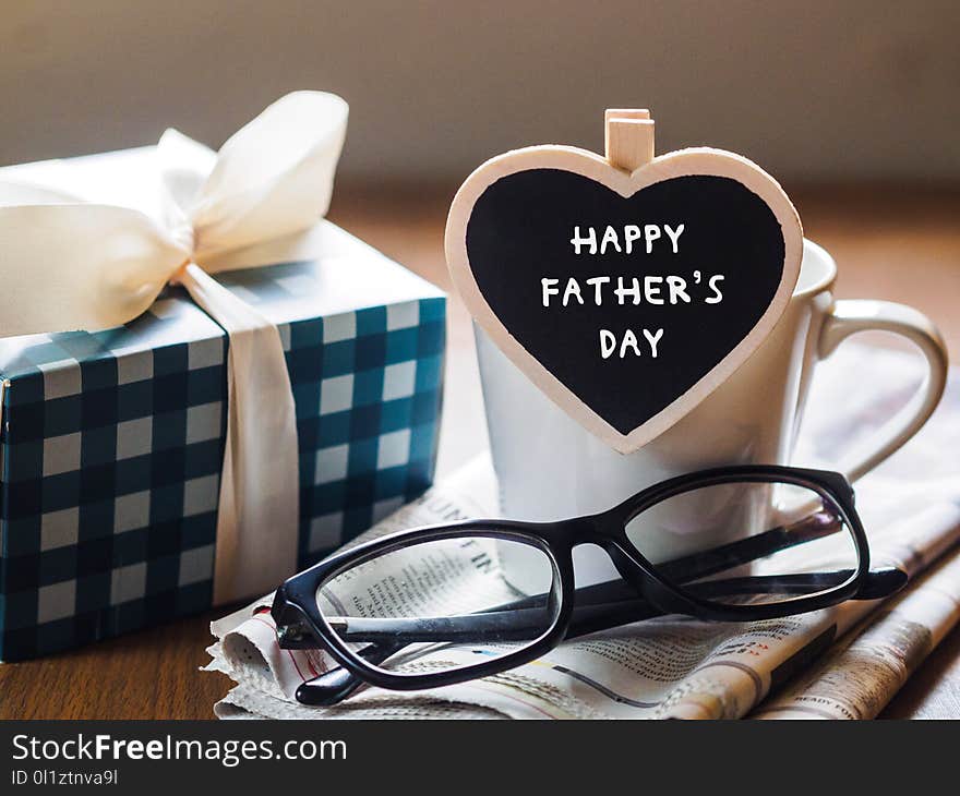 Happy fathers day concept. coffee cup with gift box, heart tag with Happy father`s day text and newspaper, glasses on wooden table background.