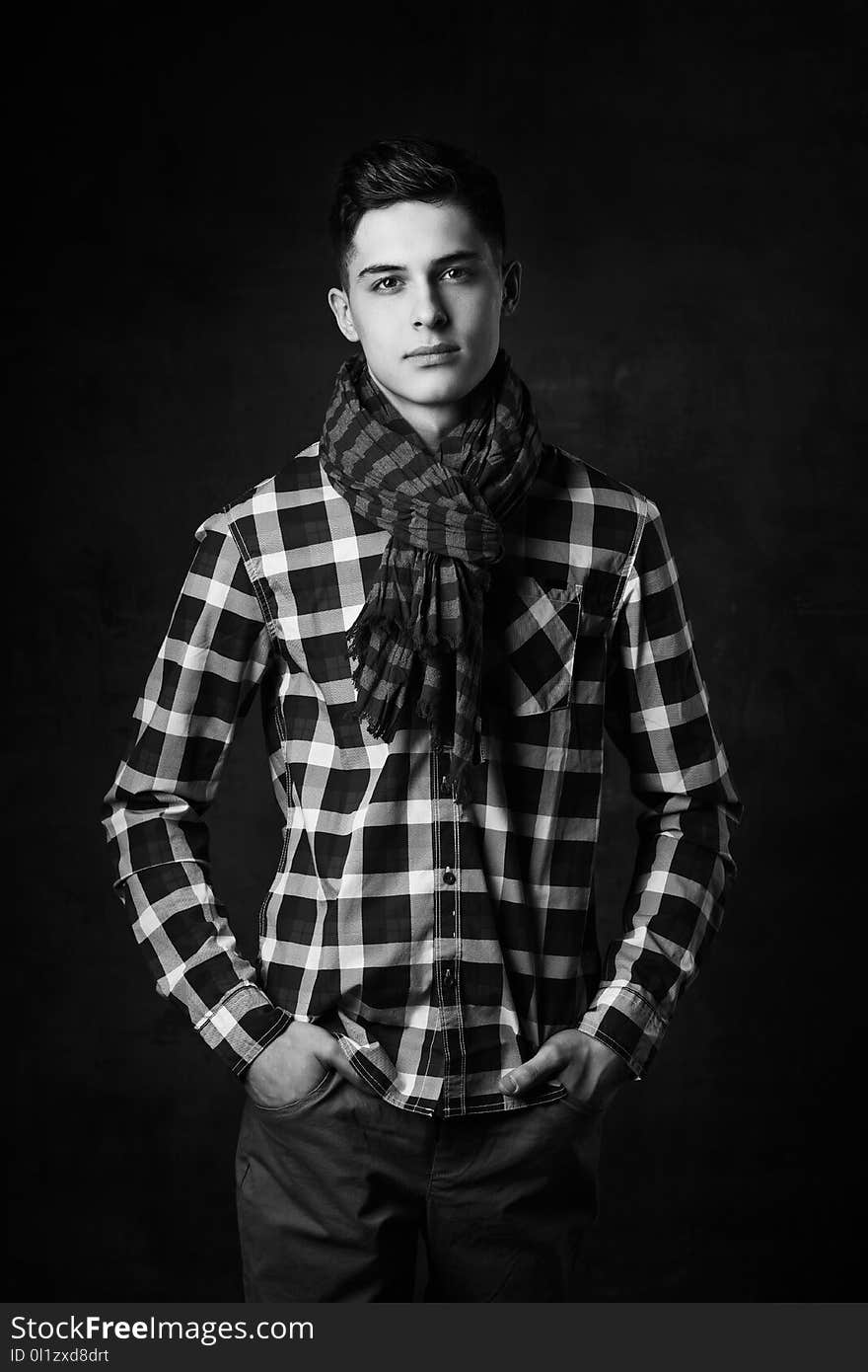 Portrait of young trendy handsome man with short dark hair wearing checkered shirt and brown trousers standing and posing against gray concrete wall. Portrait of young trendy handsome man with short dark hair wearing checkered shirt and brown trousers standing and posing against gray concrete wall