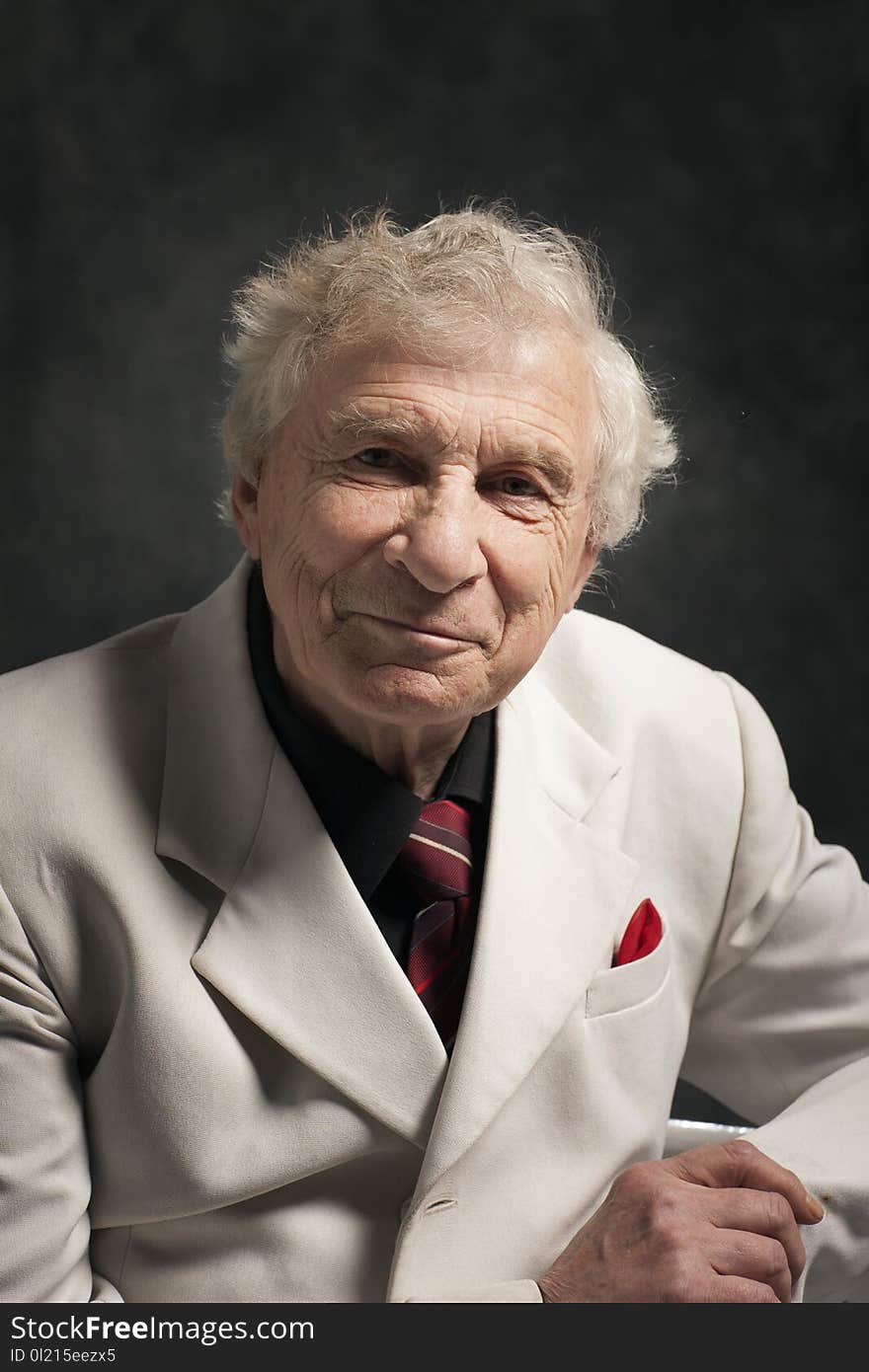 Portrait of a senior charismatic man in a white suit with a black shirt and red tie on a gray background. Portrait of a senior charismatic man in a white suit with a black shirt and red tie on a gray background