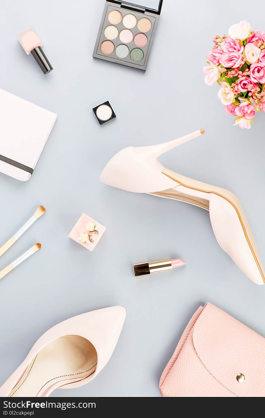 Fashion blogger workspace flat lay with pumps, cosmetics, purse, planner book and flowers.