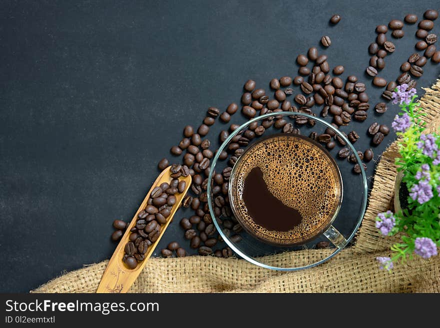 Espresso coffee in glass cup. glass cup of espresso coffee with coffee bean on traditional sack textile. cup of coffee on black table and coffee bean in burlap sack and flower