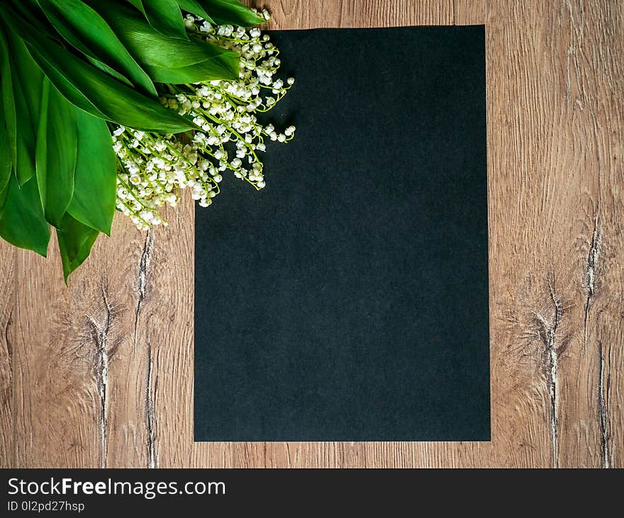 Bouquet of lilies of the valley on a wooden background and an empty piece of black paper.