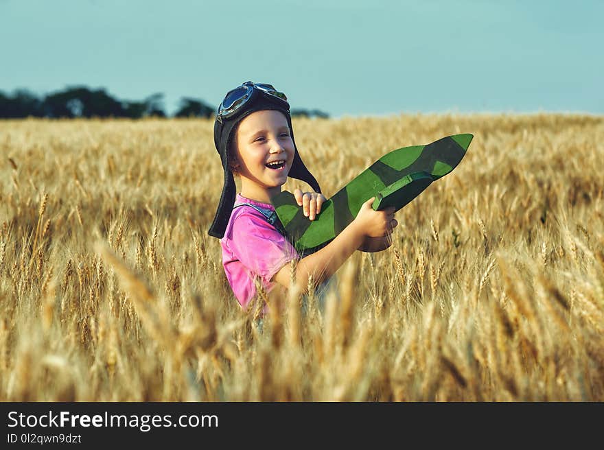 Cheerful girl in a field of wheat playing with a model aircraft