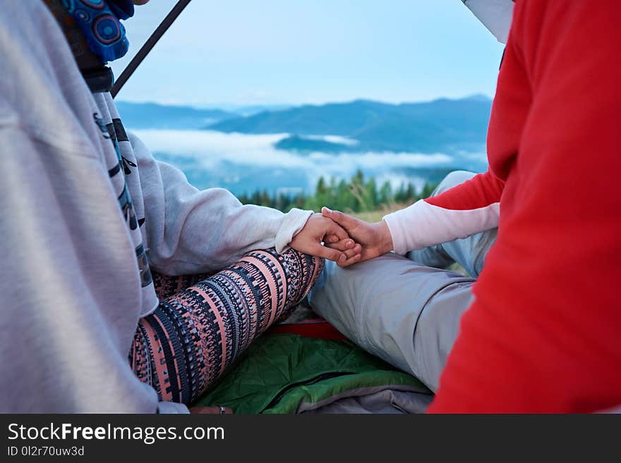 Close-up of guy and girl holding hands sitting in tent on blurred background of mountains in light haze and blue sky. Romantic holiday in the mountains. Close-up of guy and girl holding hands sitting in tent on blurred background of mountains in light haze and blue sky. Romantic holiday in the mountains