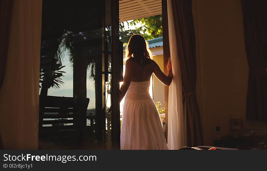 Brunette girl stands in the doorway in the early morning during sunrise with lens flare effects