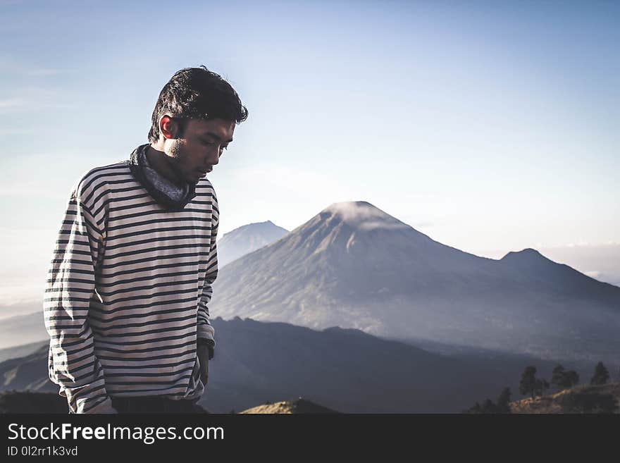 Person Wearing White and Black Striped Sweatshirt Standing in Front of Mountains